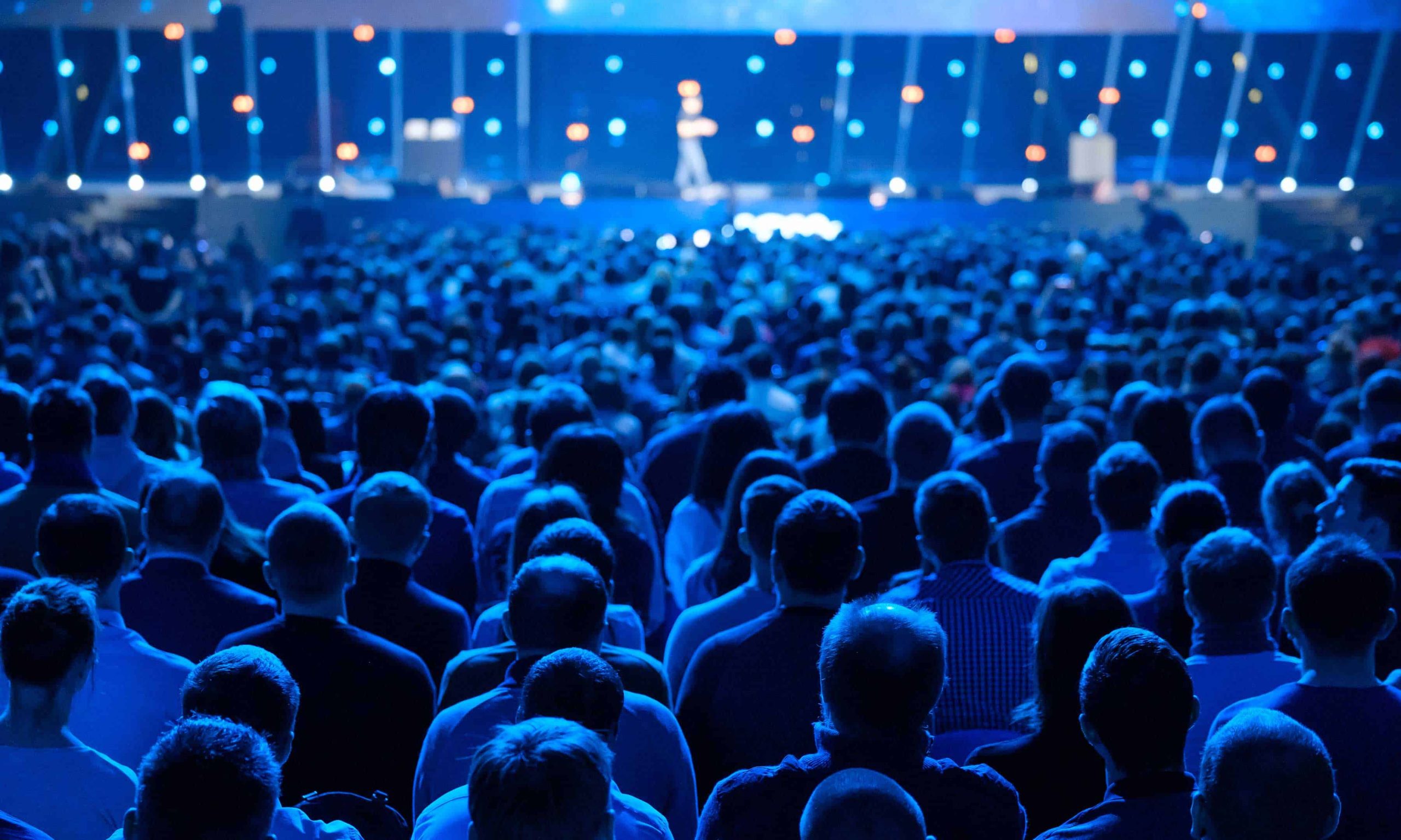Evento em auditório no formato de palestra, com várias pessoas sentadas e olhando para o palco.